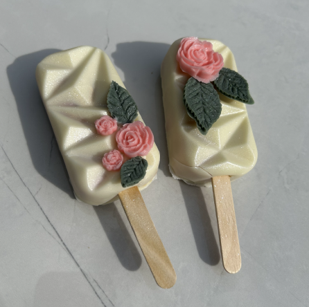 Two white cake pops with pink rose decorations.